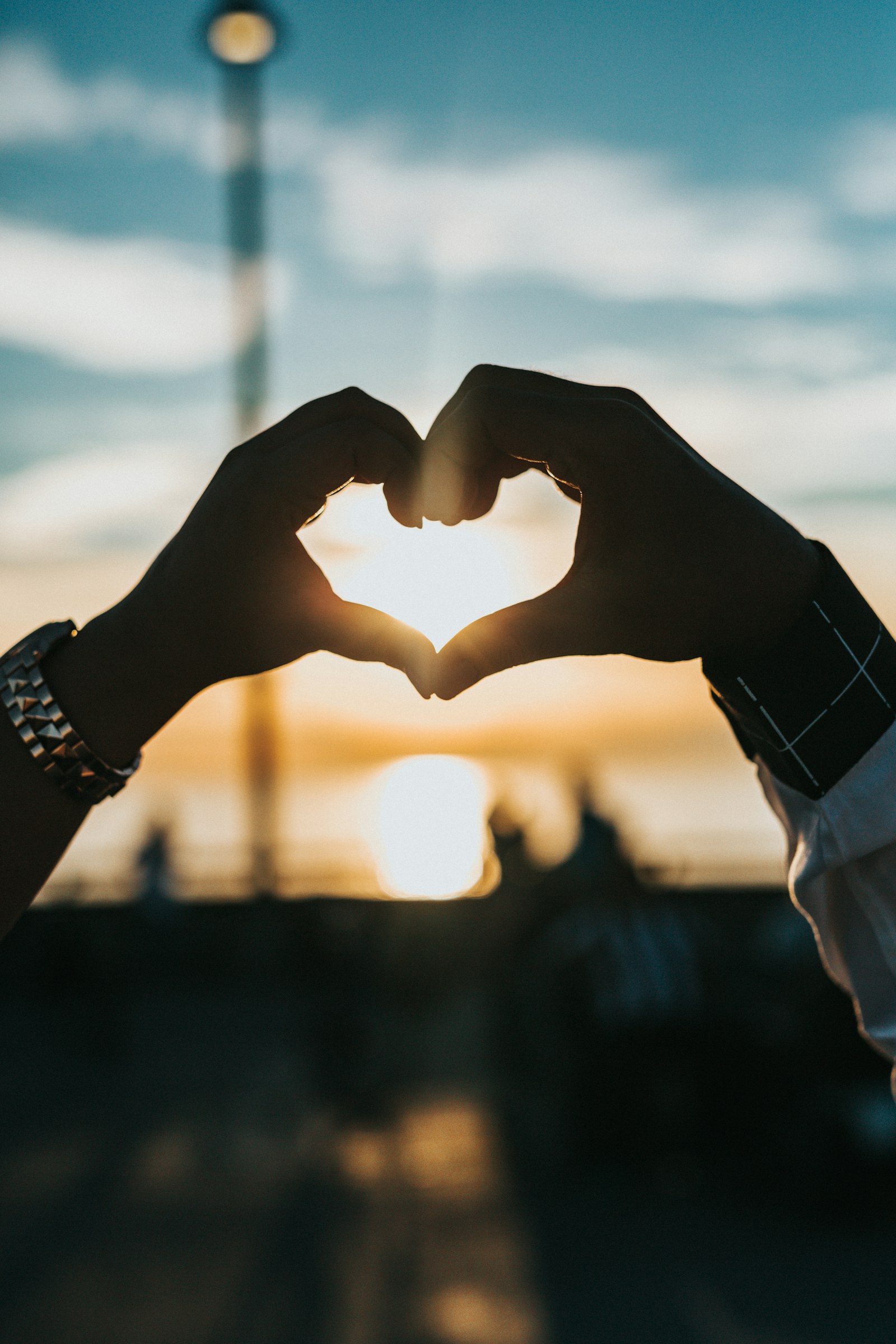 Two people shape a heart with their hands in the evening light.